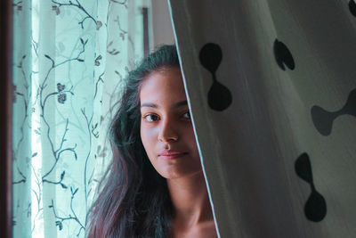 Portrait of teenage girl standing by curtain at home