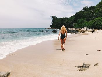 Rear view of woman on beach against sky