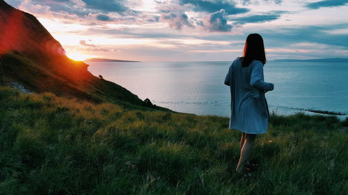 Woman walking at sea shore against sky during sunset