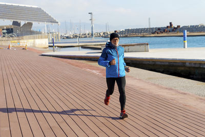 Senior man in sport clothes jogging on harbour dock in a sunny day