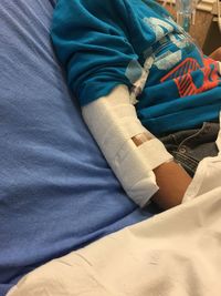 Midsection of boy with broken hand lying on bed