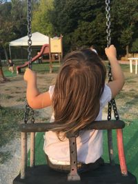 Rear view of girl sitting on swing at playground