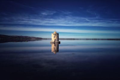 Reflection of lighthouse in sea against sky