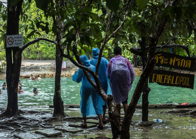 People wearing raincoat while standing by sign board hanging from branch at emerald pool