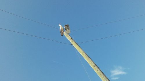 Low angle view of telephone pole against clear blue sky