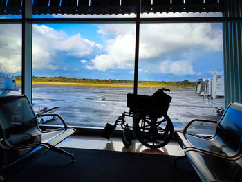 Chairs and table by sea against sky seen through window