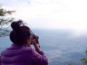 Rear view of woman photographing landscape against sky