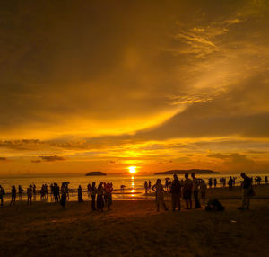 Silhouette people on beach against sky during sunset