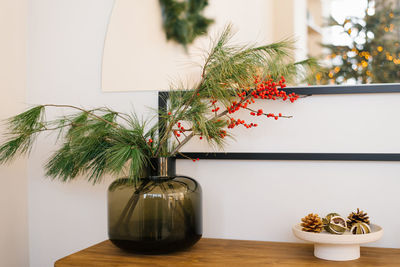 Pine branches and red berries in a glass jar vase. christmas decor in the interior of a cozy house