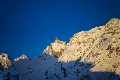 Low angle view of snowcapped mountains against clear blue sky