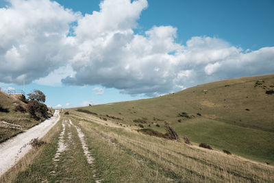 Empty road amidst field against sky