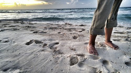 Low section of person standing on sea shore during sunset