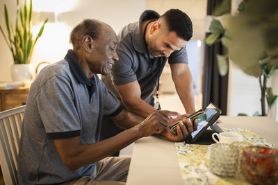 Male nurse assisting senior man in using digital tablet and smart phone at nursing home