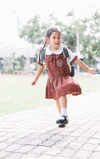 Full length of schoolgirl looking away while running on footpath