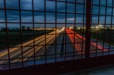 Road by illuminated bridge in city against sky during sunset