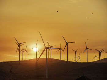 Silhouette wind turbines on land against sky during sunset