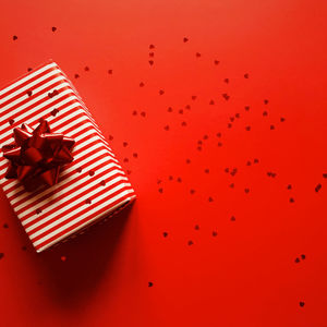 Directly above shot of gift box and heart shape confetti on red background