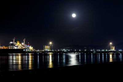 Illuminated city by sea against sky at night