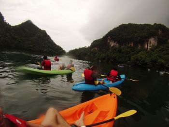 People sitting on riverbank against sky