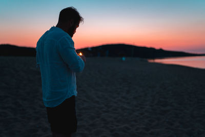 Man standing on beach against sky during sunset