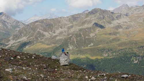 Mature man sitting on rock formation against mountains