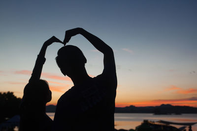 Silhouette couple making heart shape against sky during sunset