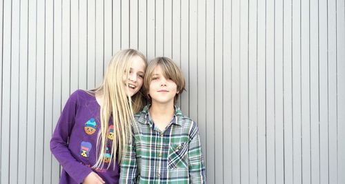 Happy siblings standing against patterned wall