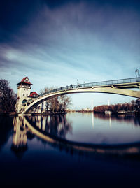 Bridge over river by buildings against sky