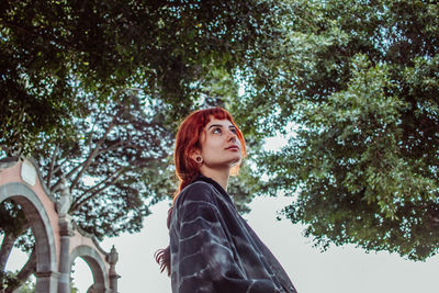 Low angle portrait of woman standing against trees