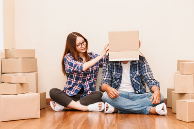Woman putting box on boyfriend while sitting on floor at new home