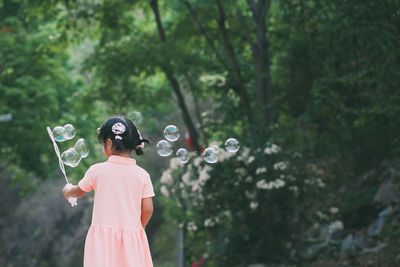 Girl holding bubble wand while standing against trees