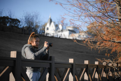 Woman sitting on railing against bare trees during winter