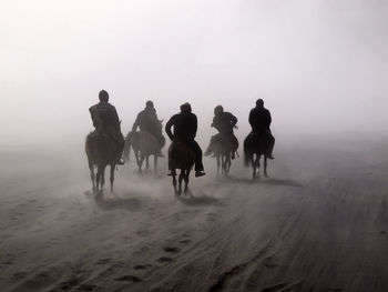 People walking on sand dune in desert against sky