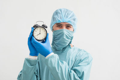 Portrait of surgeon holding alarm clock while standing against white background
