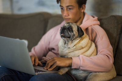 Teenage boy using laptop while holding dog at home