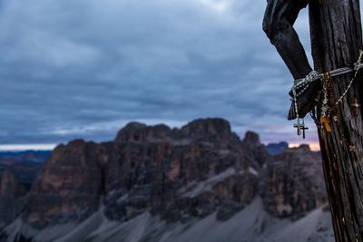 Crosses hanging on crucifix by rocky mountains against cloudy sky