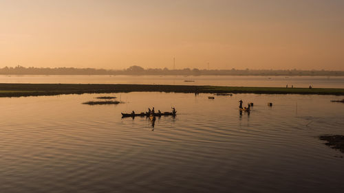 Silhouette people boating on river against sky during sunset