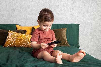 Cute boy using phone while sitting on bed at home