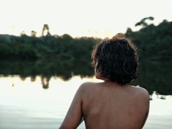 Rear view of shirtless man at lake against sky during sunset