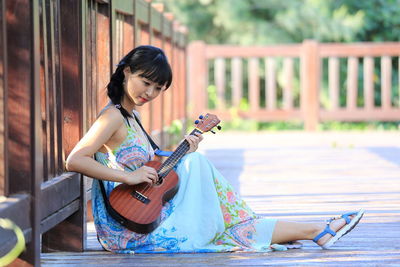 Beautiful woman playing guitar while sitting on hardwood floor