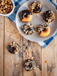 Chocolate glazed donuts with hazelnuts on wooden background, top view