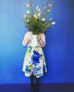 Rear view of woman holding flower vase while standing against blue wall