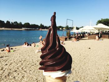 Close-up of ice cream cone at beach against sky on sunny day