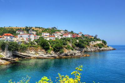 Scenic view of sea by buildings against clear blue sky