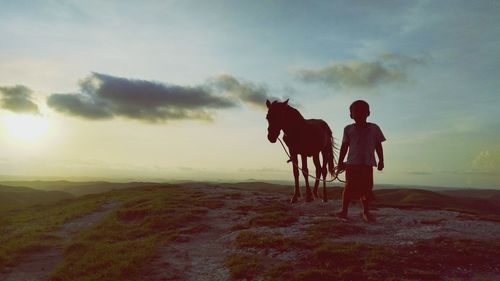 Rear view of men standing on land against sky during sunset