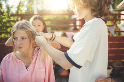 Friends braiding teenage girl's hair in back yard