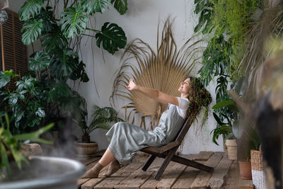 Satisfied calm woman florist relaxing in indoor garden enjoy mental balance and wellbeing at home