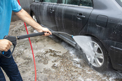 Mature man cleaning automobile with foam shampoo chemical detergents during carwash self service