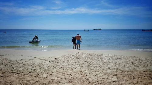 Rear view of people walking on beach against sky