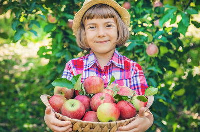Portrait of smiling cute girl holding basket of apples